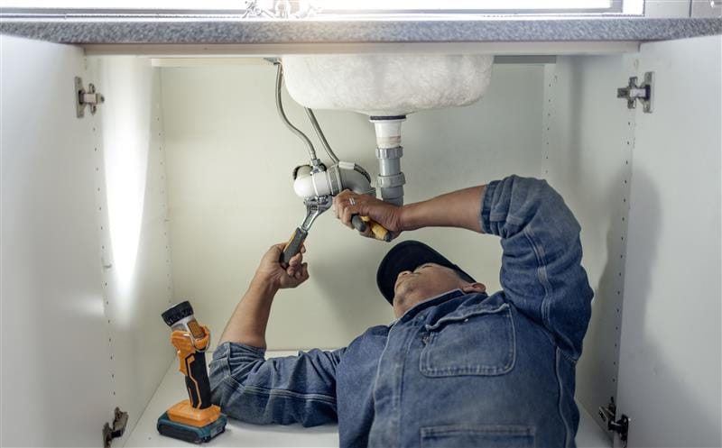 Plumber repairing pipes beneath a bathroom sink in North Highlands